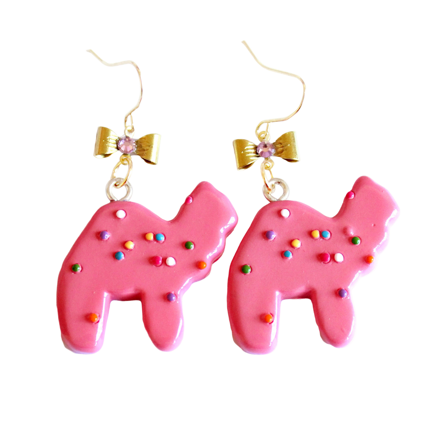 A pair of earrings featuring pink animal cookie charms with multicolored sprinkles, attached to gold-colored hooks with bows adorned with pink crystals.