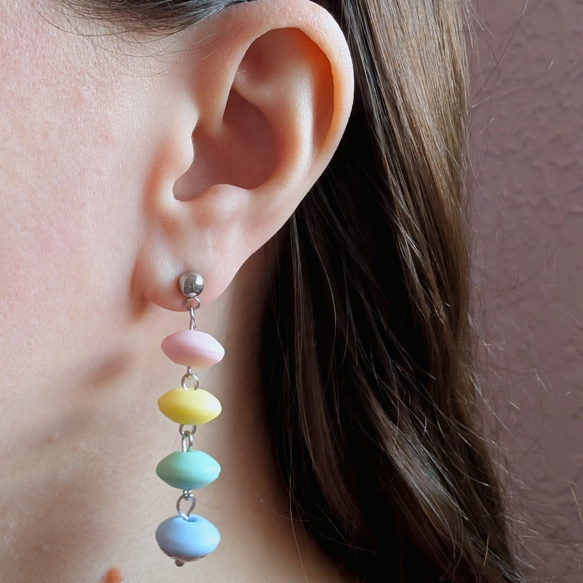 Model photography showcasing the scale and lightweight drape of the asymmetric pastel faux candy earrings with pink resin bow and cascading 12mm matte clay beads.