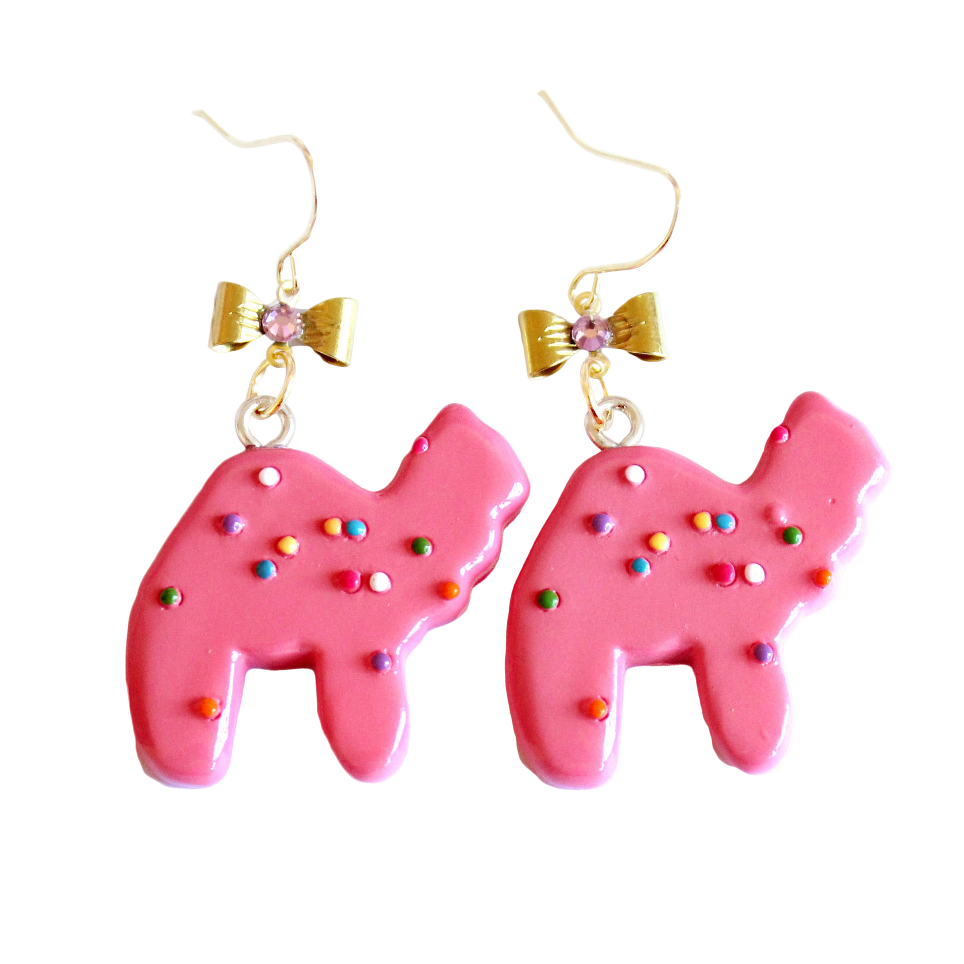 A pair of earrings featuring pink animal cookie charms with multicolored sprinkles, attached to gold-colored hooks with bows adorned with pink crystals.