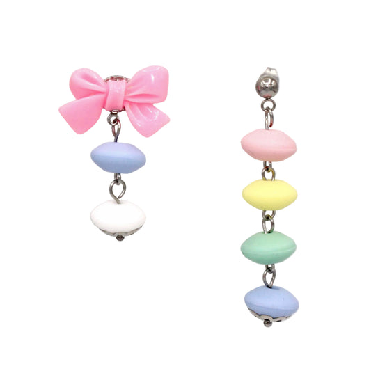Asymmetrical pastel candy statement earrings featuring a glossy pink resin bow drop post and a long four-tier vertical cascading rainbow strand on a seamless white background.